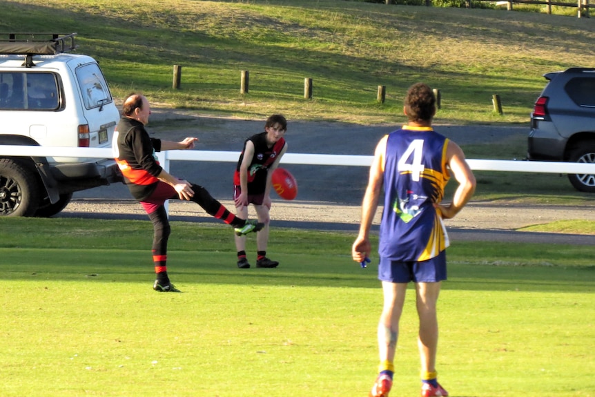 A man in red and black football uniform kicks a Sherrin