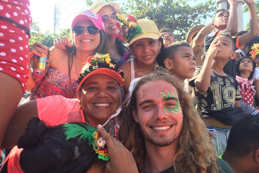 A young tourist with shoulder-length hair wearing face paint smiles with a group of locals at a festival.