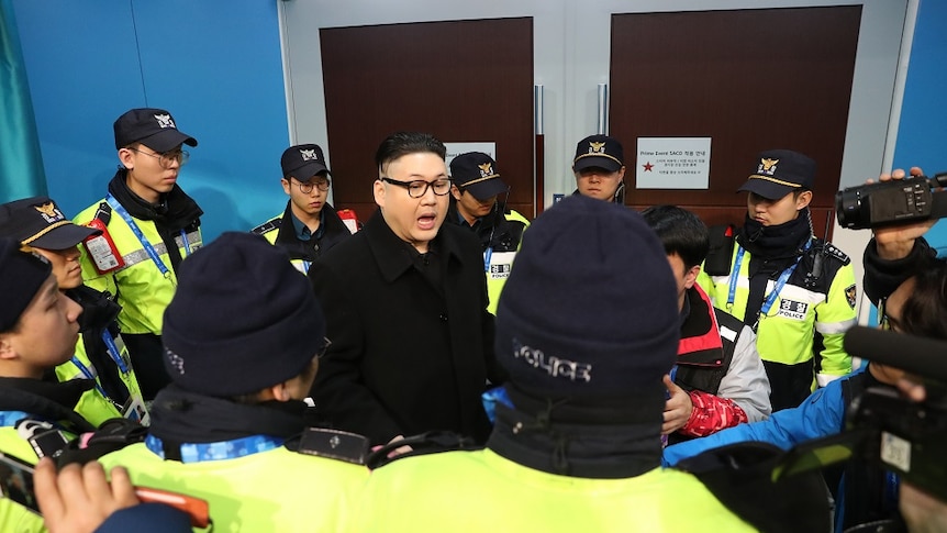 A man impersonating Kim Jong Un is surrounded by security personnel.