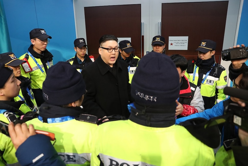 A man posing as Kim Jong Un is surrounded by security personnel.