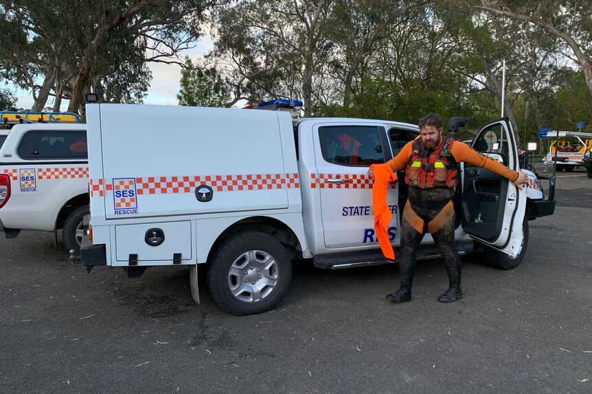 A man wearing an orange outfit with waders steps from a truck