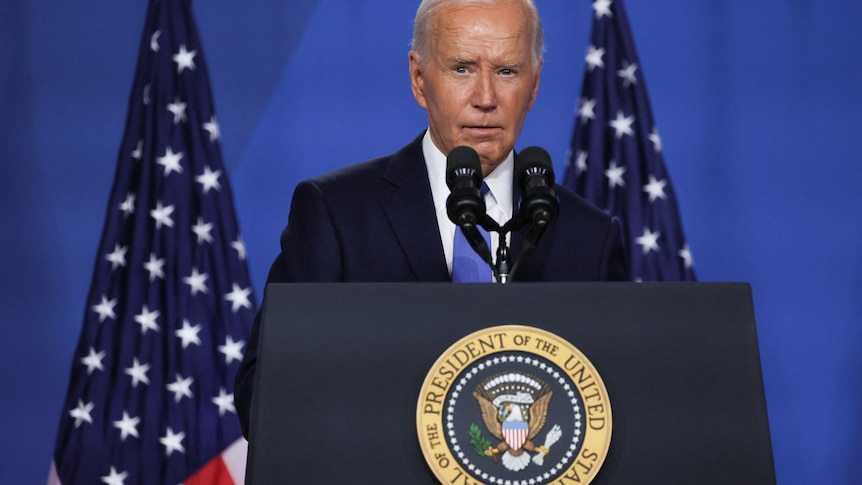 Biden speaks from behind a lectern with american flags behind him