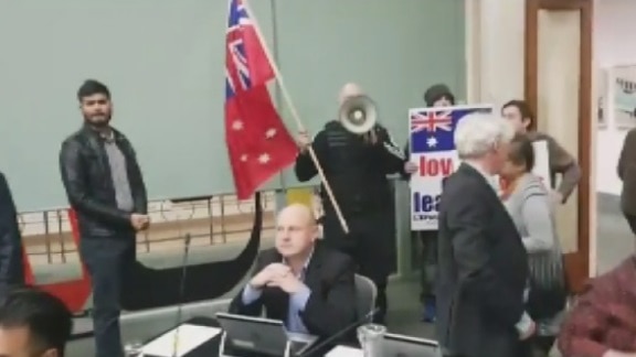 Far-right protesters holding flags and signs disrupt a Yarra Council meeting