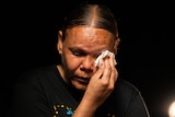 An Indigenous lady wipes away tears from her face with a tissue