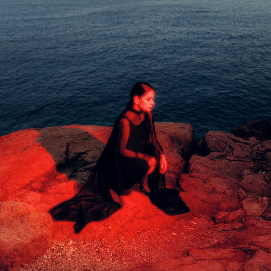 a woman sits on a cliff above the ocean