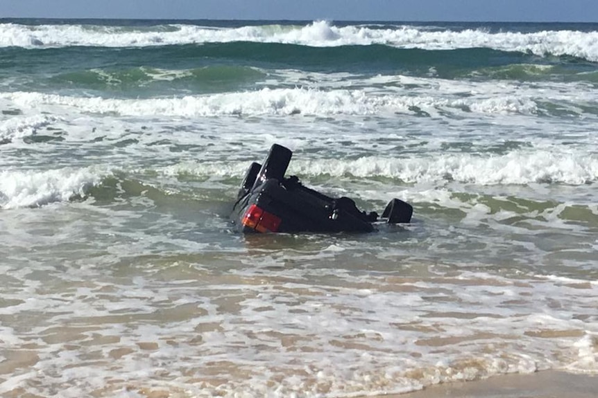 A car upside down being hammered by waves on Fraser Island