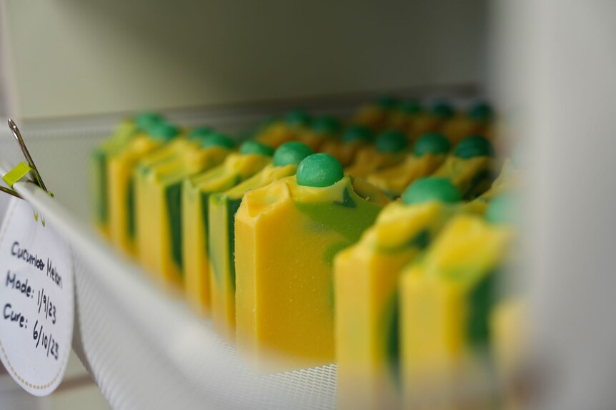 Blocks and green and yellow homemade soap sit in rows on a shelf.