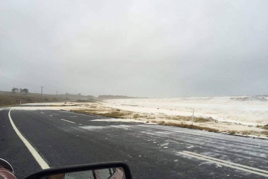 Rough waves break over a road in east Tasmania