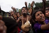 A Rohingya man stretches his arms out for food distributed by local volunteers. He is surrounding by other people doing the same