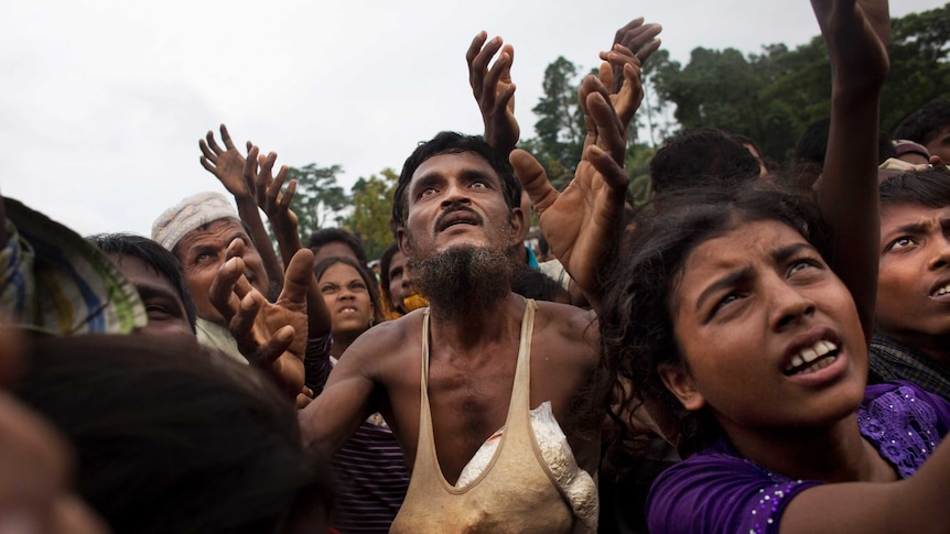 A Rohingya man stretches his arms out for food distributed by local volunteers. He is surrounding by other people doing the same