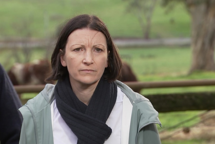 A woman wearing a scarf and jacket standing in front of a paddock