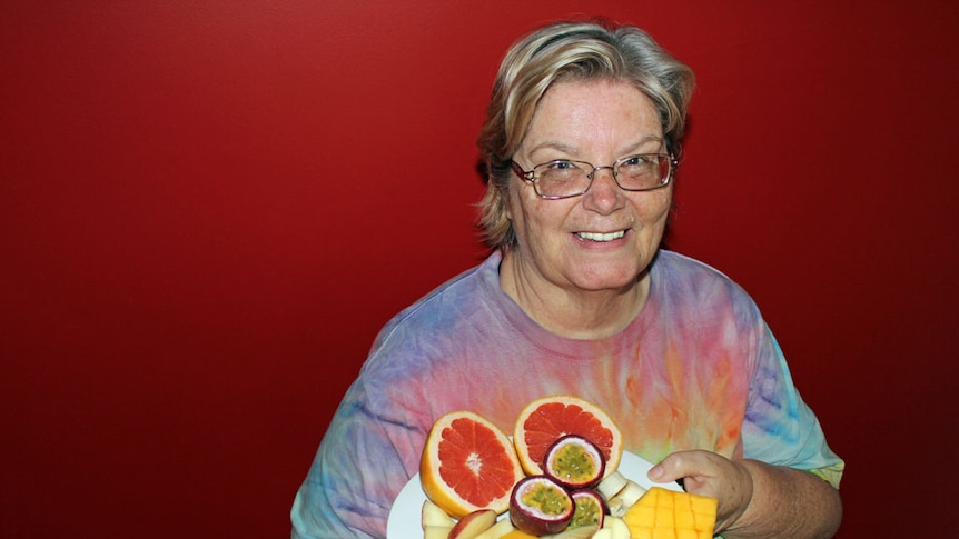 61 year old woman smiling holding plate of cut up fruit