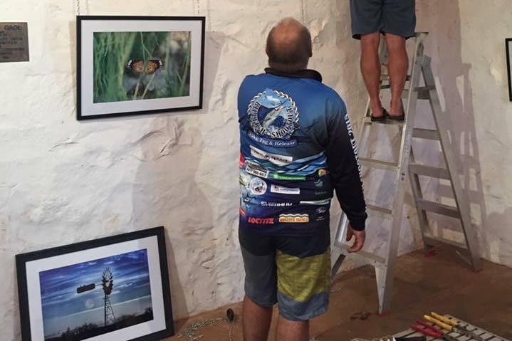 Two men hanging photos on a wall.