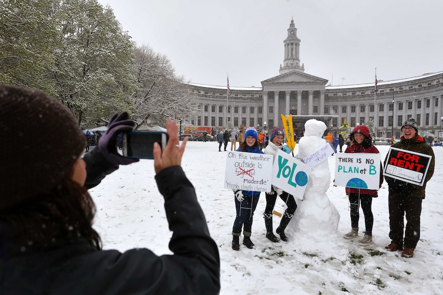 Four people hold climate change signs nxext to a snowman in Denver