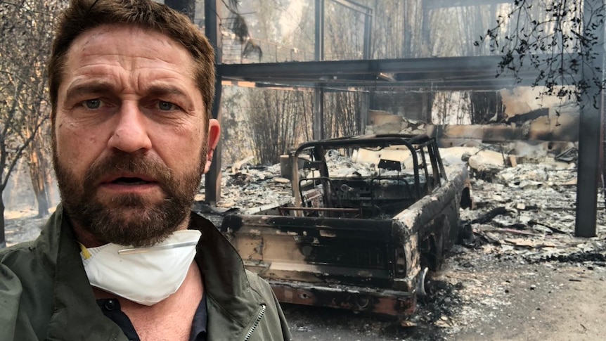 A selfie of Gerard Butler shows the burnt remains of his home and a car in the background