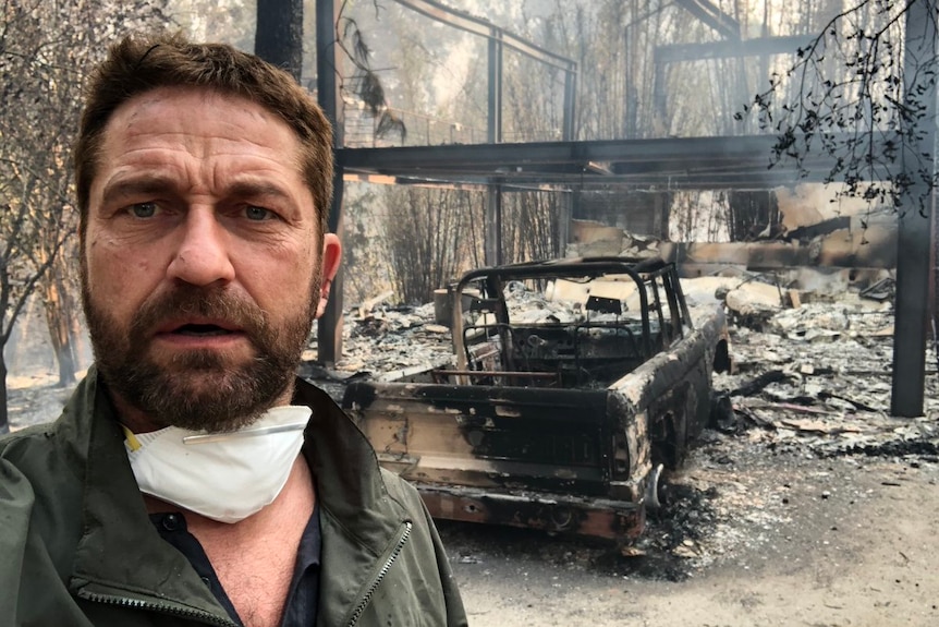 A selfie of Gerard Butler shows the burnt remains of his home and a car in the background