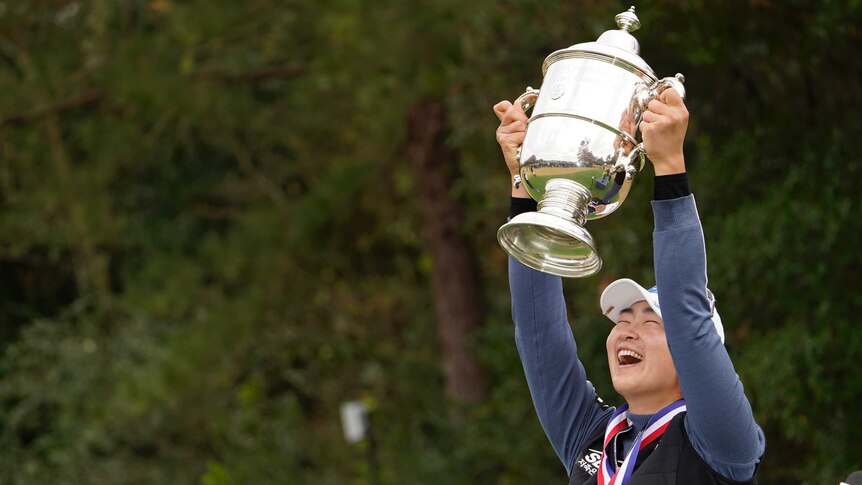 A Lim Kim lifts the US Women's Open trophy above her head while smiling and wearing a medal.