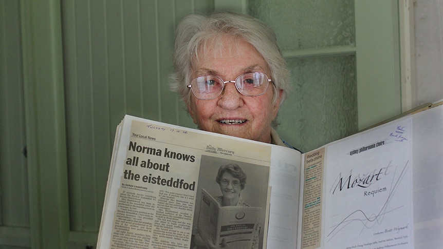Norma Shuttlewood holding a newspaper clipping that reads 'Norma knows all about the eisteddfod'