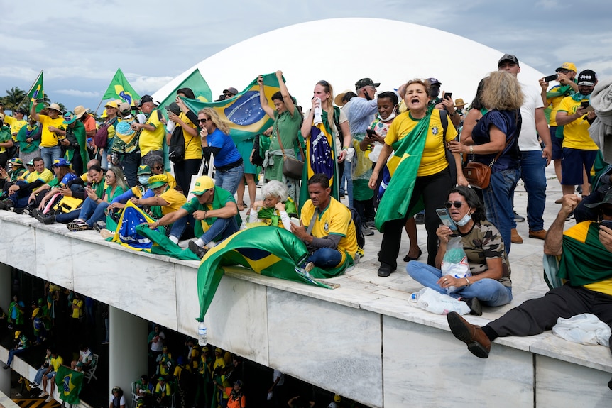 Protesters dressed in yellow shirts hold green flags while standing and sitting on a roof.