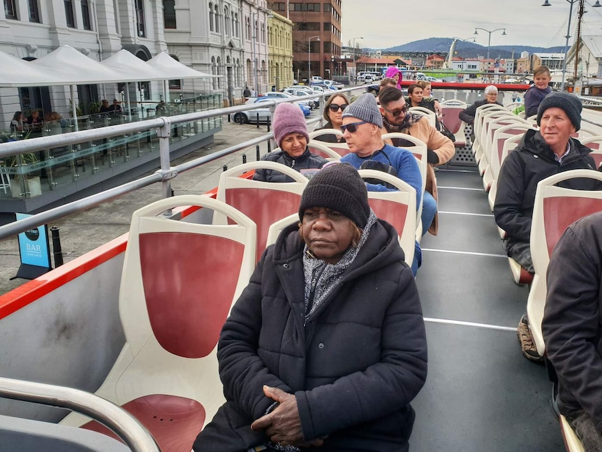 A group of people sit in an open-top bus during a tour of Hobart.