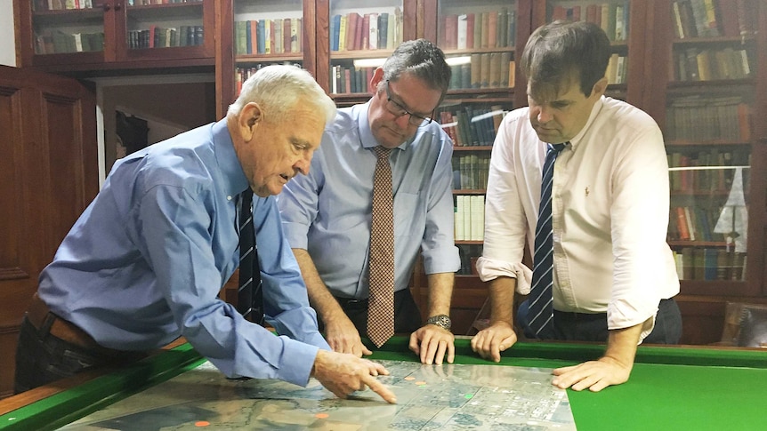 Three men inspect a large map