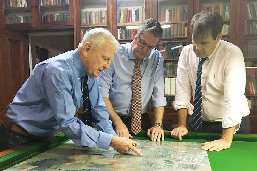 Three men inspect a large map