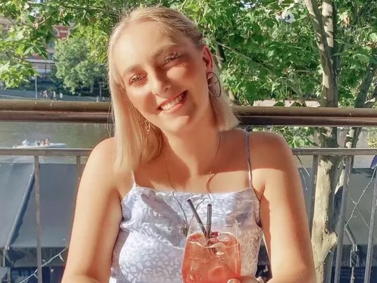 Hannah sitting in the sun smiling with a drink in hand.