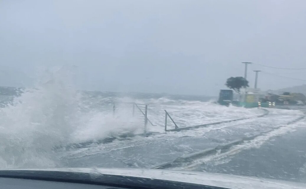 a big wave of white water smashes over a road in the midst of a storm