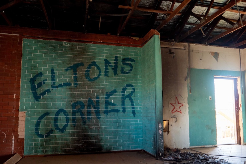 A blue brick wall is tagged 'Eltons Corner' and a pile of burnt debris lays on the ground.