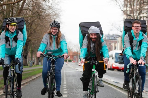Four Deliveroo workers wearing aqua ride bicycles while delivering food.
