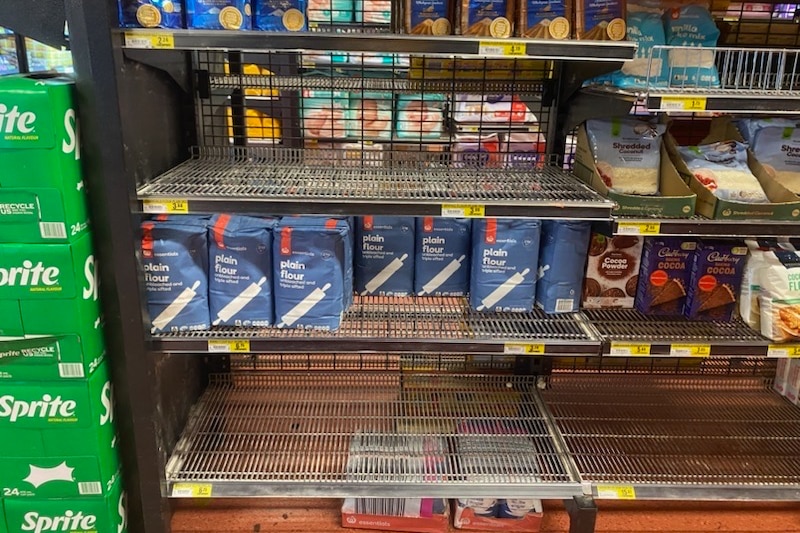 a bare grocery shelf with bags of flour