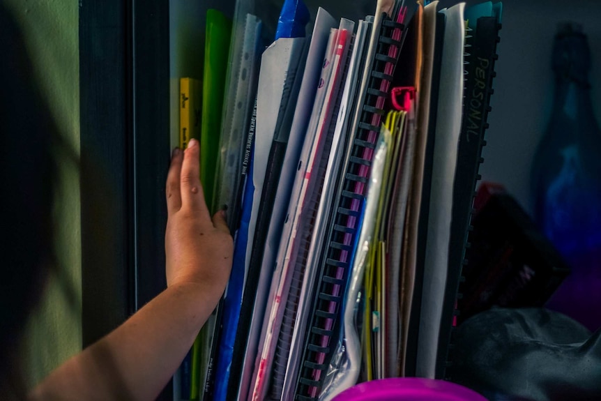A child's hands flicks through colourful school binders in a cupboard.