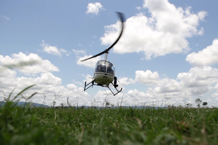 A helicopter hovers over short grass.