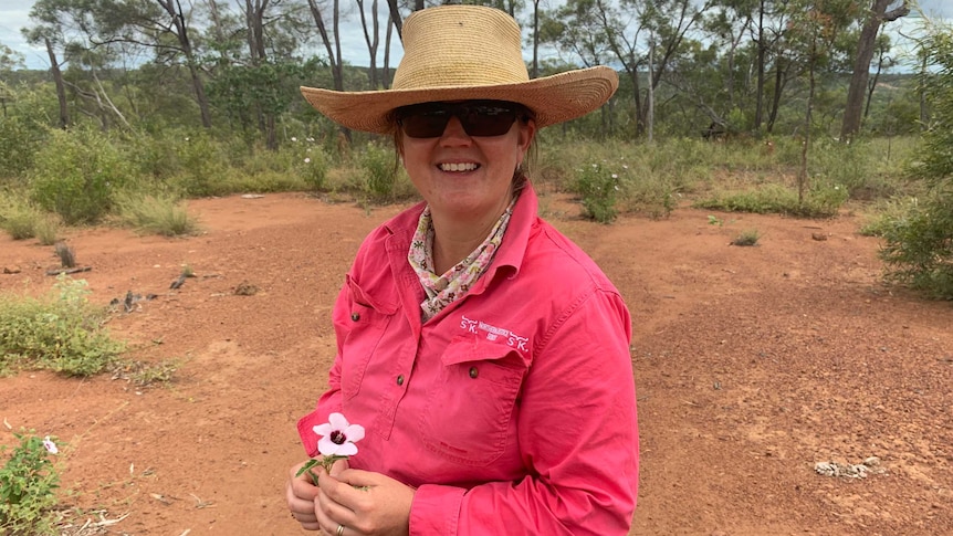 A smiling woman standing on a farm, wearing a straw hat.