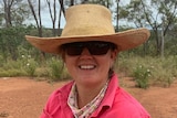 A smiling woman standing on a farm, wearing a straw hat.