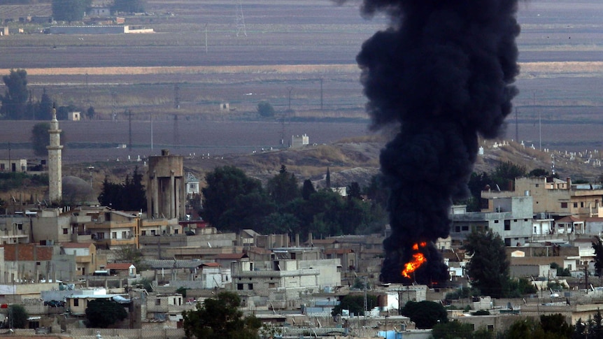 Black smoke rises and flames can be seen from above a Kurdish town in Syria.