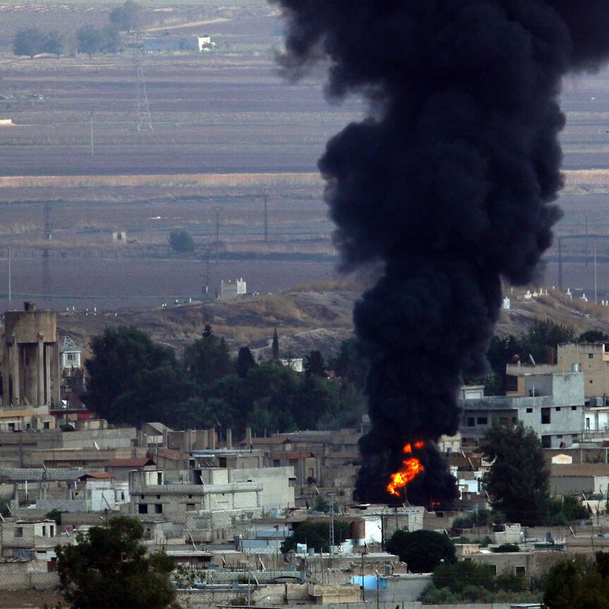 Black smoke rises and flames can be seen from above a Kurdish town in Syria.