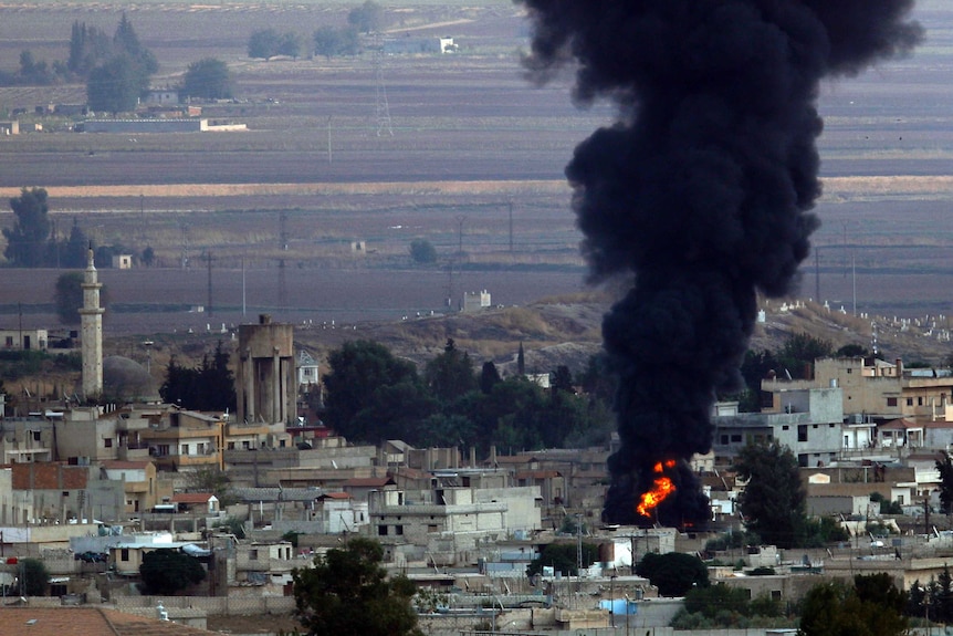 Black smoke rises and flames can be seen from above a Kurdish town in Syria.