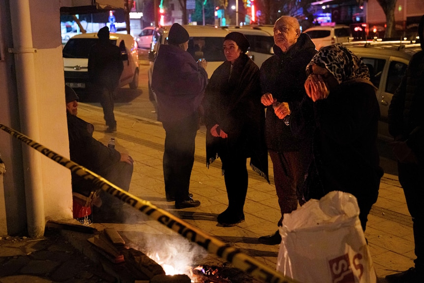 People stand near police tape at night 