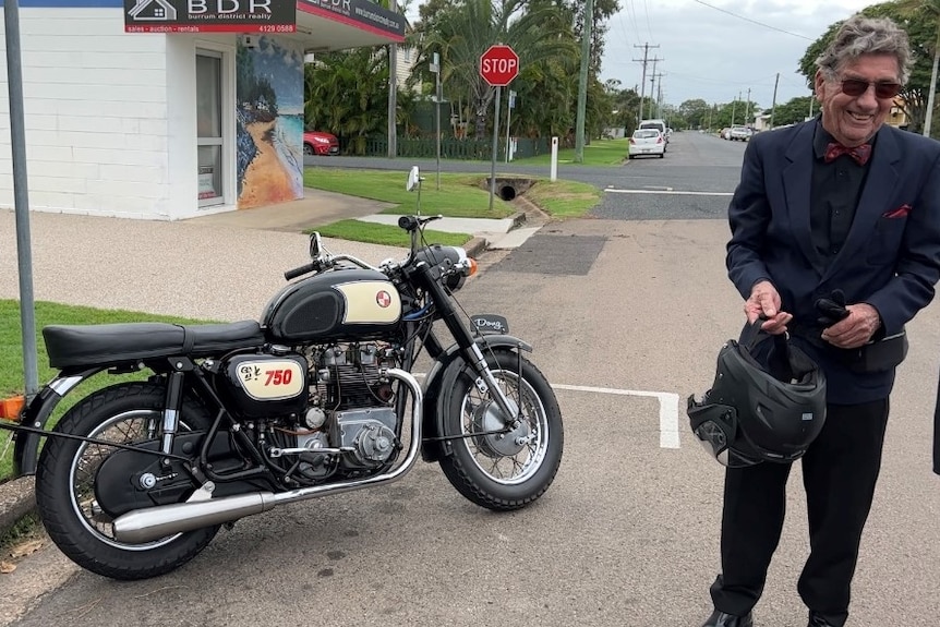 A man in a suit smiles next to a motor bike