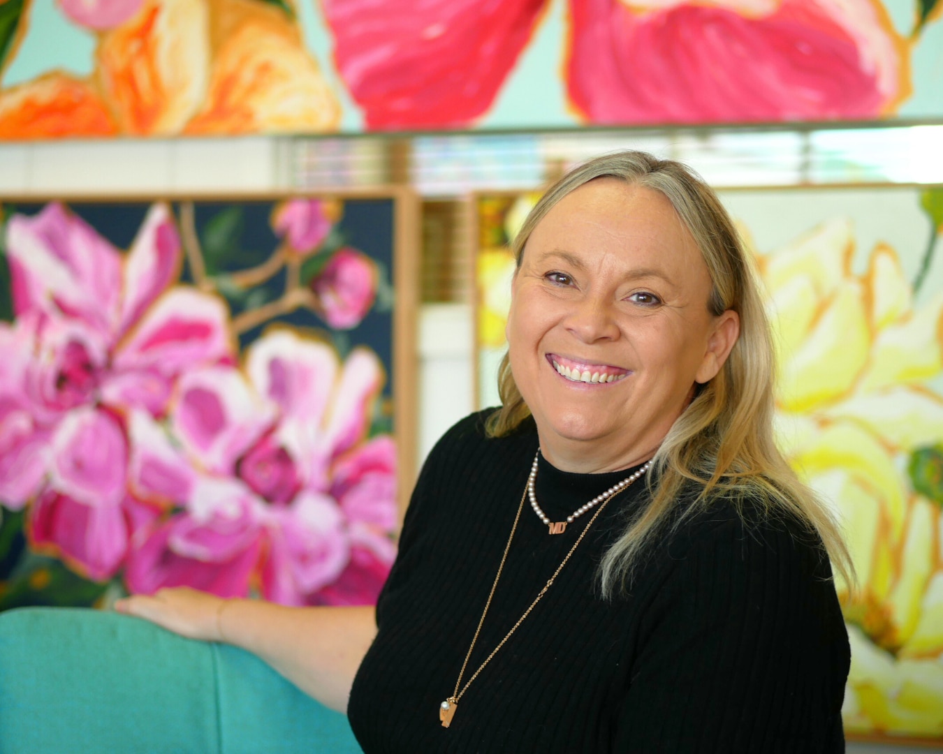 a woman smiling with various colourful paintings situated behind her