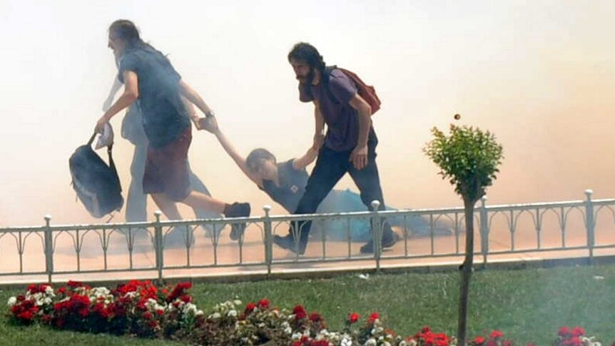 Demonstrators help one another as Turkish riot policemen use tear gas to disperse clashes