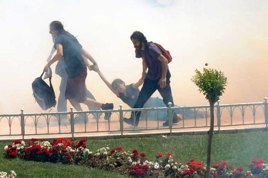 Demonstrators help one another as Turkish riot policemen use tear gas to disperse clashes