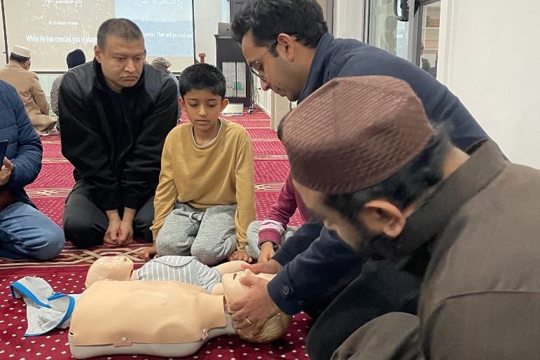 A man demonstrates CPR on a plastic dummy to a group of men in a room