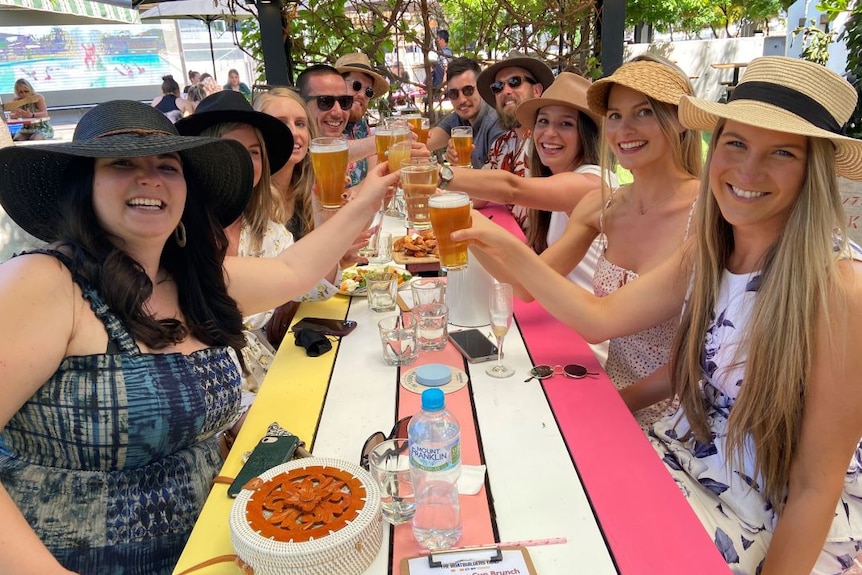 A group of 10 friends sit at a long table and raise their glasses.