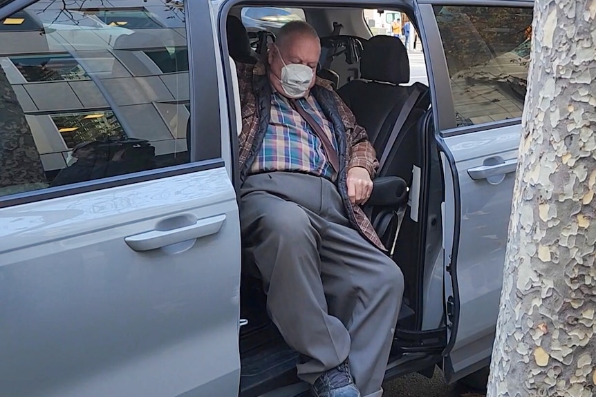 Hutchins wears a covid face mask and is getting out of the rear passenger seat of a van