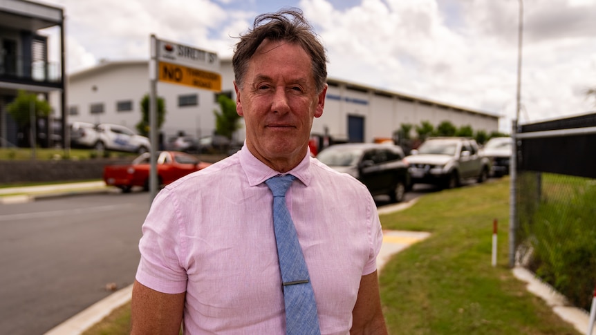 a man in a pink shirt and blue tie standing on a suburban street