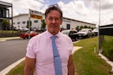a man in a pink shirt and blue tie standing on a suburban street