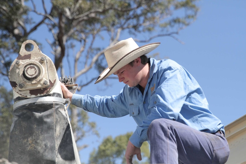 Cameron Saul rests on one knee on top of a feeder as stockfeed is being loaded into the feeder