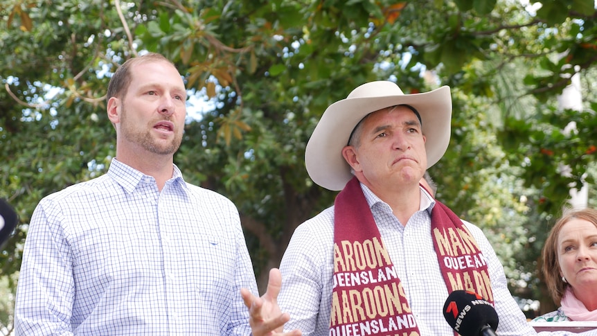 Two male politicians wearing light blue button downs. One wears a cowboy hat and a maroons scarf. 